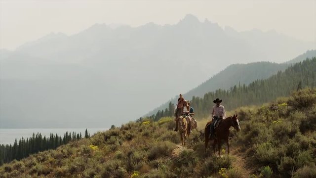 Wide shot of friends horseback riding near lake / Redfish Lake, Idaho, United States