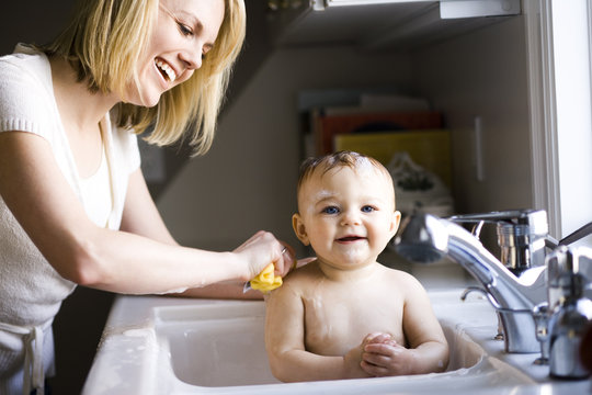 Smiling mother bathing baby girl in sink