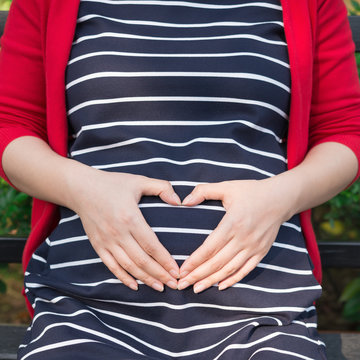 young pregnant woman putting hands on belly, shaped like a heart