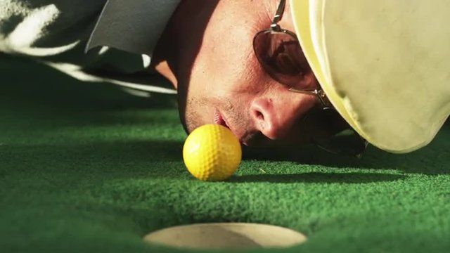 CU Man lying on golf course green blowing golf ball towards hole, Orem, Utah, USA