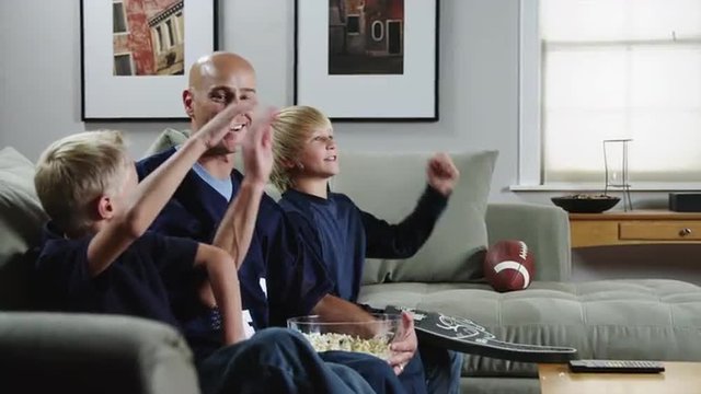 MS DS Father with two sons (8-9, 10-11) watching match in TV and eating popcorn / Orem, Utah, USA
