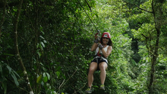 Medium low angle tracking shot of woman ziplining to landing in forest / Quepos, Puntarenas, Costa Rica