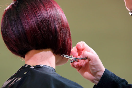 Hairdresser trimming red hair with scissors