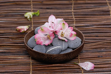  orchid with gray stones in wooden bowl with petals on mat 