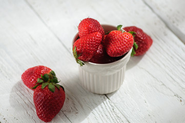 Strawberry in ceramic cup on white wooden background