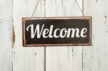 Old metal sign in front of a white wooden wall - Welcome