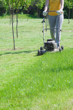 Young female in yard - pushing grass trimming lawnmower