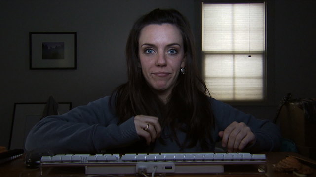 A young woman at a keyboard picking her nose