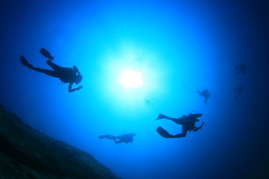 Scuba diving underwater: divers silhouette and sun