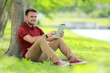 college student sitting under the tree while playing a tablet