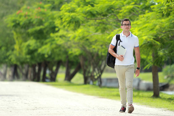 handsome college student walking by at college park with backpac