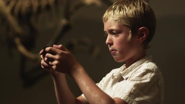 CU R/F Boy (10-11) playing game boy in natural history museum, dinosaur's skeleton in background, Lehi, Utah, USA