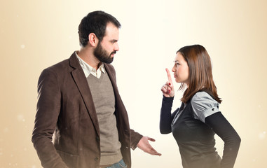 Young girl making silence gesture at her boyfriend over white ba