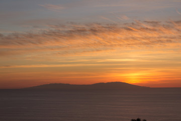 Fototapeta na wymiar Island silhouette sunset with orange sky and clouds