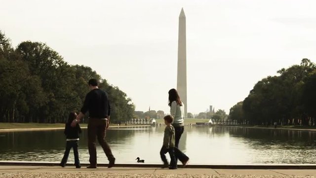 WS Family with two children (4-5, 6-7) relaxing by reflecting pool, Washington Monument in background, Washington D.C, USA