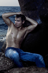 Sexy boy sits on a rock in the sea.