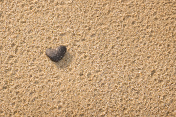 Fototapeta na wymiar One Black stone shaped heart on the beach