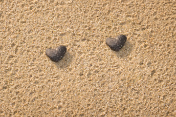 Fototapeta na wymiar Two black stone shaped heart on the beach