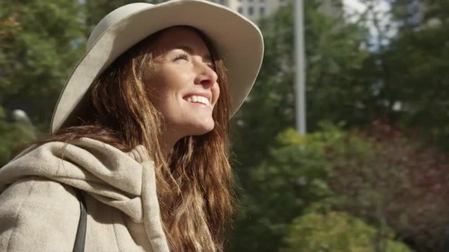 Close up tracking shot of smiling young woman looking up at trees and highrises / New York City, New York, United States