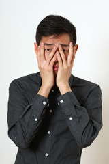 Frustrated young Asian man covering his face with palms