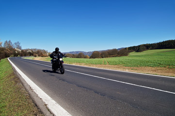 Black motorcycle traveling on the road in rural landscape