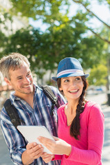 A young loving couple is holding a tablet in the city.