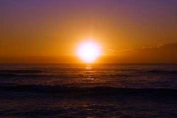 Naklejka na ściany i meble Sunrise over the ocean with waves rolling toward shore