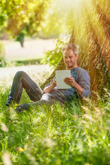 Naklejka na ściany i meble handsome man sitting in the grass, using a tablet