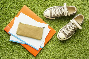Sneakers, notebooks and pen case on the lawn