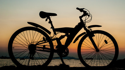 Silhouette of mountain bike parking on jetty beside sea with sun