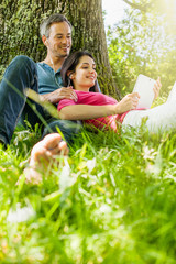 Fototapeta premium A nice couple sitting in the grass, using a tablet