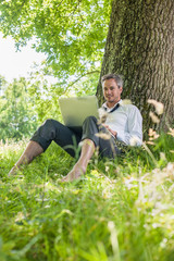 Obraz premium handsome grey hair man using a laptop, barefoot in the grass