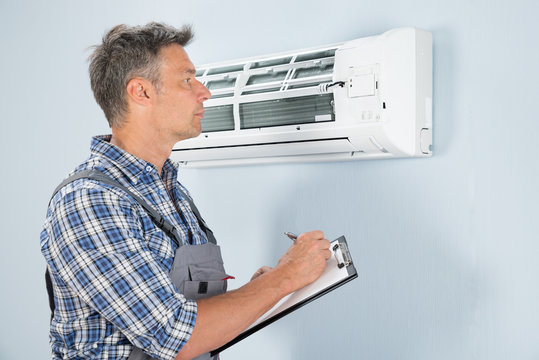 Technician With Clipboard Looking At Air Conditioner