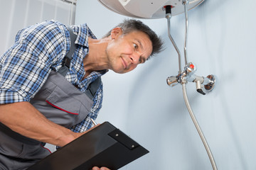 Plumber With Clipboard Looking At Electric Boiler