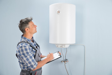 Male Plumber With Clipboard Looking At Electric Boiler