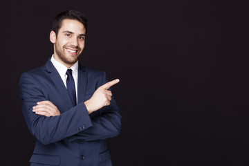Handsome business man pointing at something against dark backgro