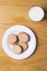 Vaso de leche con plato de galletas en superficie de madera