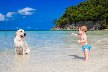 A little kid with a dog having fun on a tropical beach.