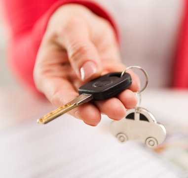A hand giving car key to buyer in automotive dealer's office