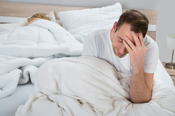 Depressed Man On Bed While Woman Sleeping