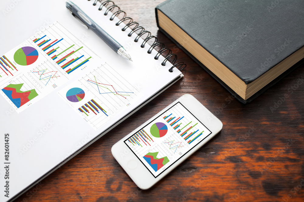 Poster analyzing graph on smart phone with notebook on office table