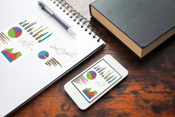 analyzing graph on smart phone with notebook on office table