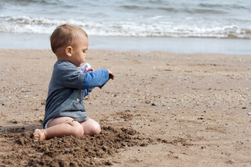 Child sitting on a beach, playing with a sand.