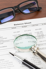 Balance sheet financial report with pen, glasses, and magnifier;