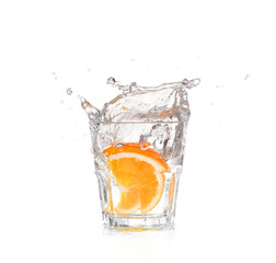 orange splashing into glass of water on white background