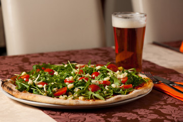 Pizza with rucola, cherry tomatoes and a glass of beer on a tebl