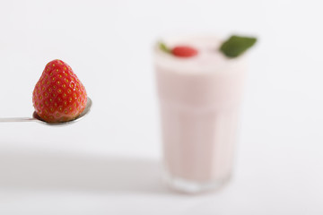Erdbeere auf einem Löffel vor einem Milchshake