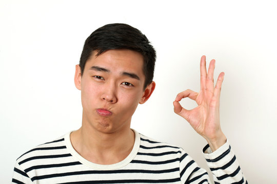 Satisfied young Asian man giving the okay sign and looking at ca