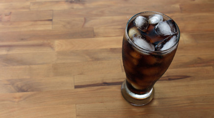 Glass of pop with ice on wooden table
