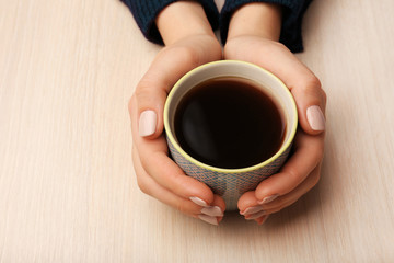 Female hands holding cup of coffee on wooden background